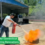 Man using fire extinguisher on open flames during a renovation safety drill outside a Connecticut home construction site now.